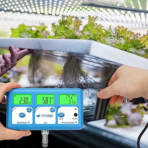 Person adjusting a digital hydroponic garden monitoring device.